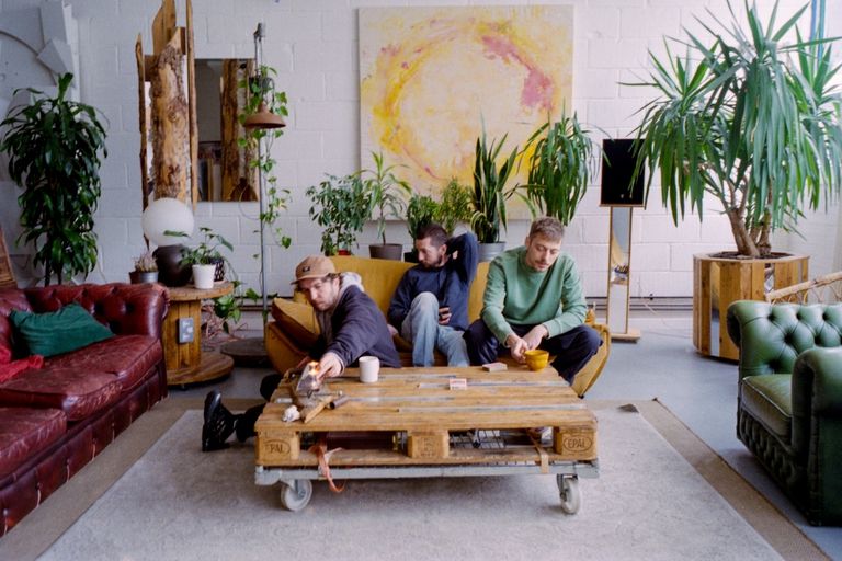 Gotts Street Park sitting around a yellow couch and wooden pallet table in a plant-filled studio space during a promo photo shoot.